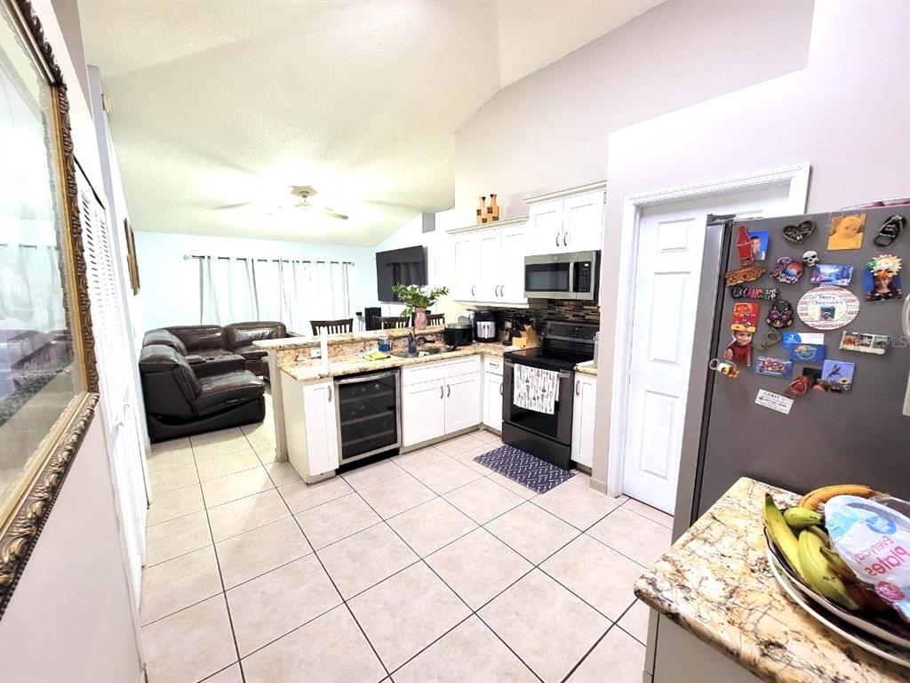 An open-concept kitchen with white cabinets and granite countertops overlooks a living room area — 1946 EXCALIBUR DRIVE, ORLANDO, FL