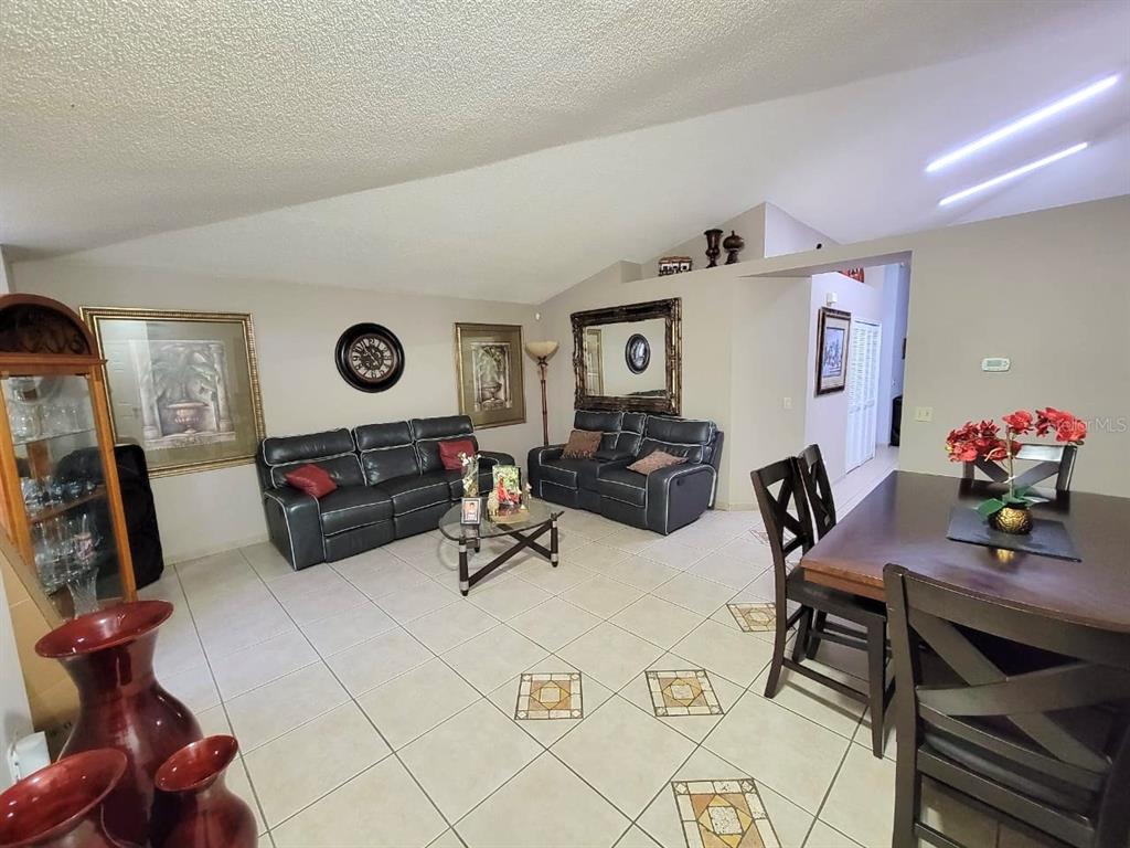 A living and dining area with tiled floors, vaulted ceilings, and dark leather furniture — 1946 EXCALIBUR DRIVE, ORLANDO, FL