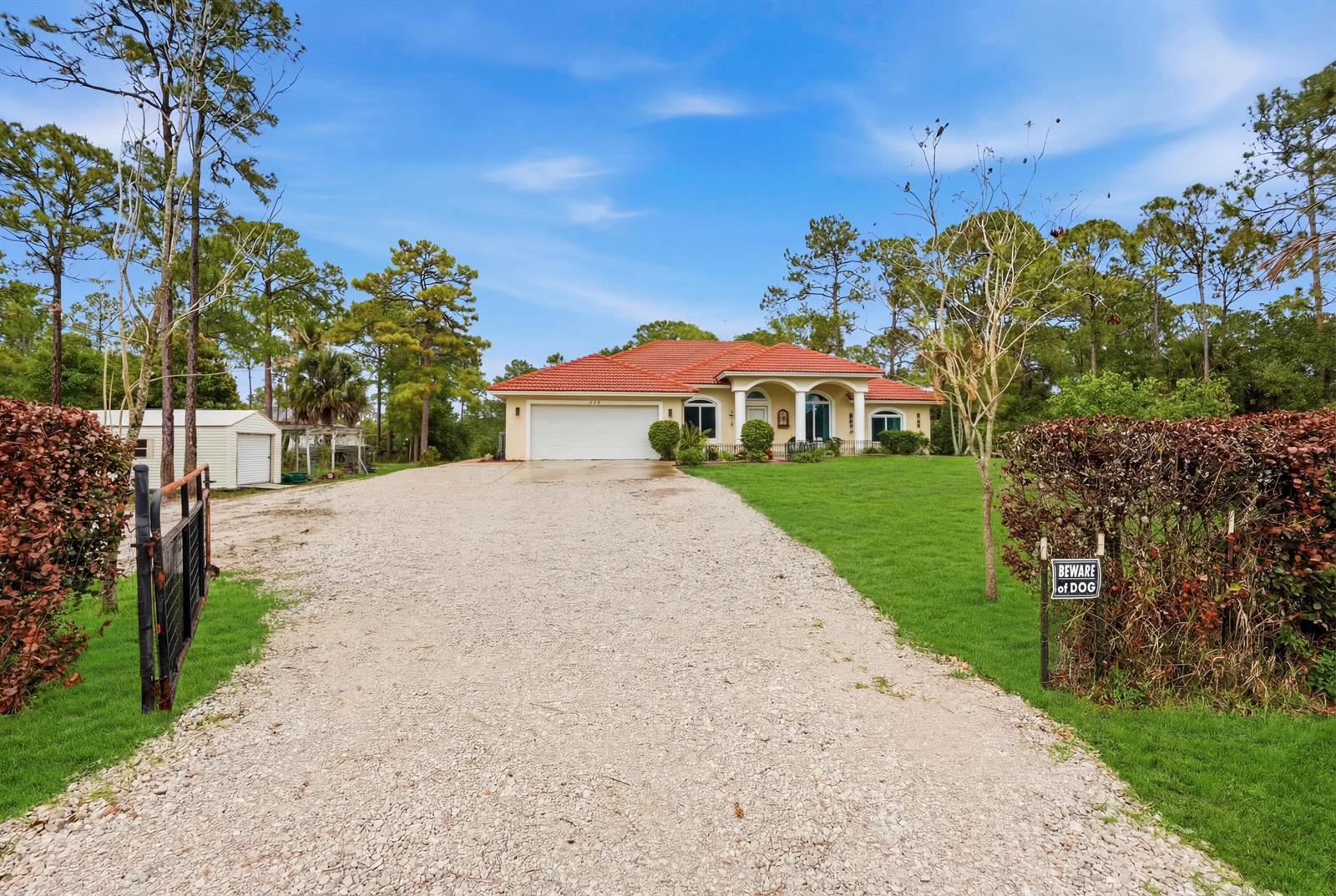A single-story house with a red tile roof sits at the end of a gravel driveway — 15327 64th Place N, FL 33470, FL