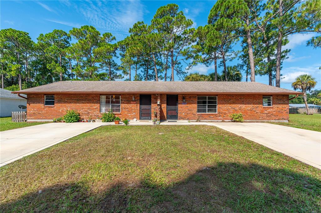 A single-story brick duplex with two front doors and separate concrete driveways under pine trees — 2304 INDIA PALM DRIVE, EDGEWATER, FL