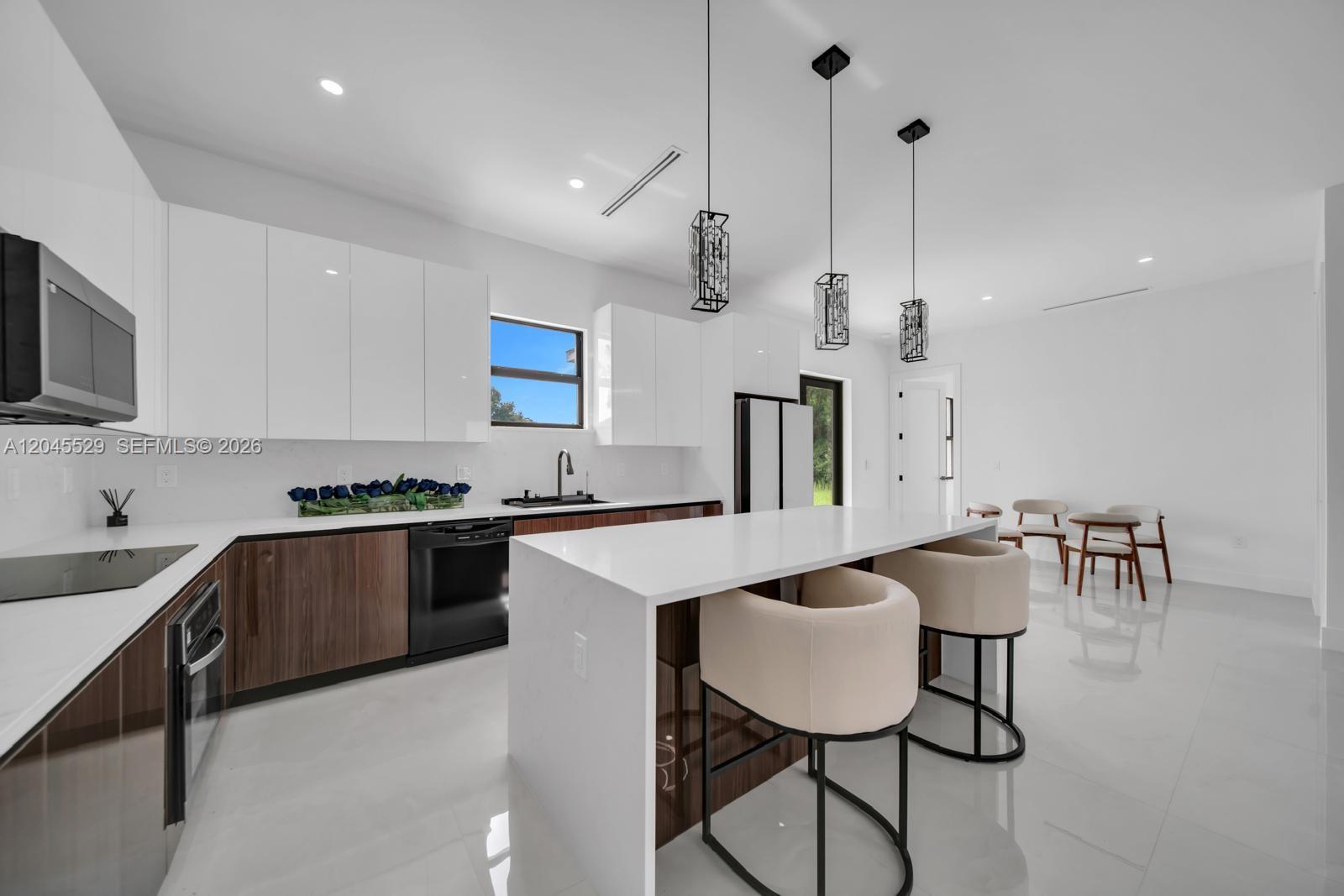 A modern kitchen features white upper cabinets, wood-toned lower cabinets, a white island, and pendant lighting — 323 LLOYD AVE S, Lehigh Acres FL 33974, LEHIGH ACRES, FL