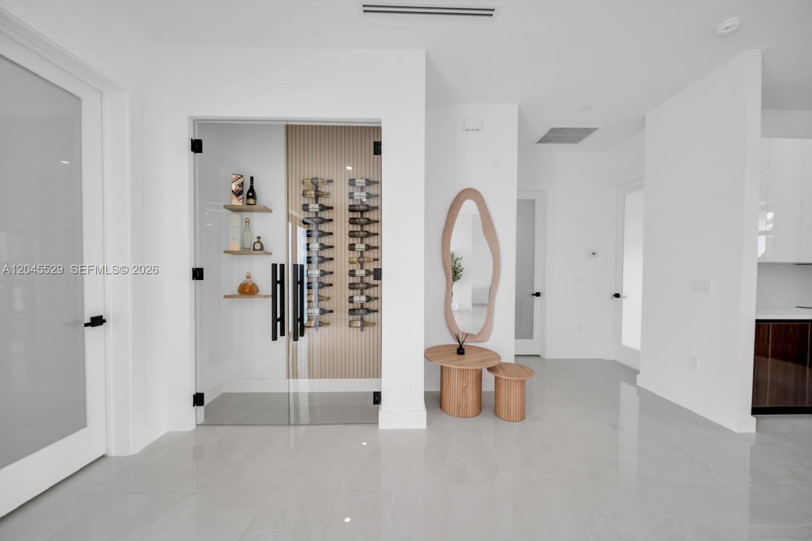 A modern interior features a glass-enclosed wine cellar, a wood-framed mirror, and light tile flooring — 323 LLOYD AVE S, Lehigh Acres FL 33974, LEHIGH ACRES, FL