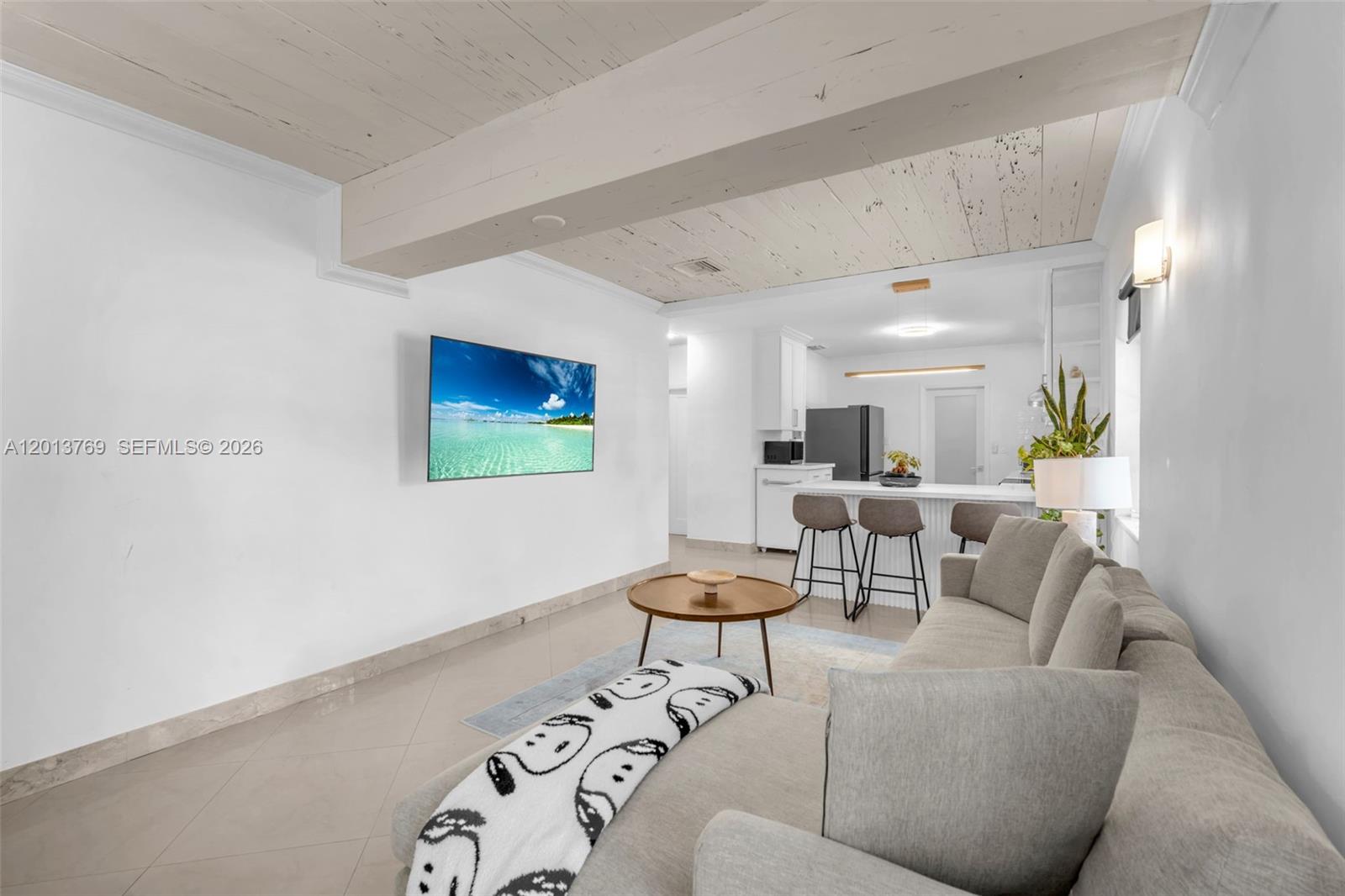 A living room with a wall-mounted television, a grey sofa, and an open kitchen — 470 NE 113th St # 1, Miami FL 33161, MIAMI, FL
