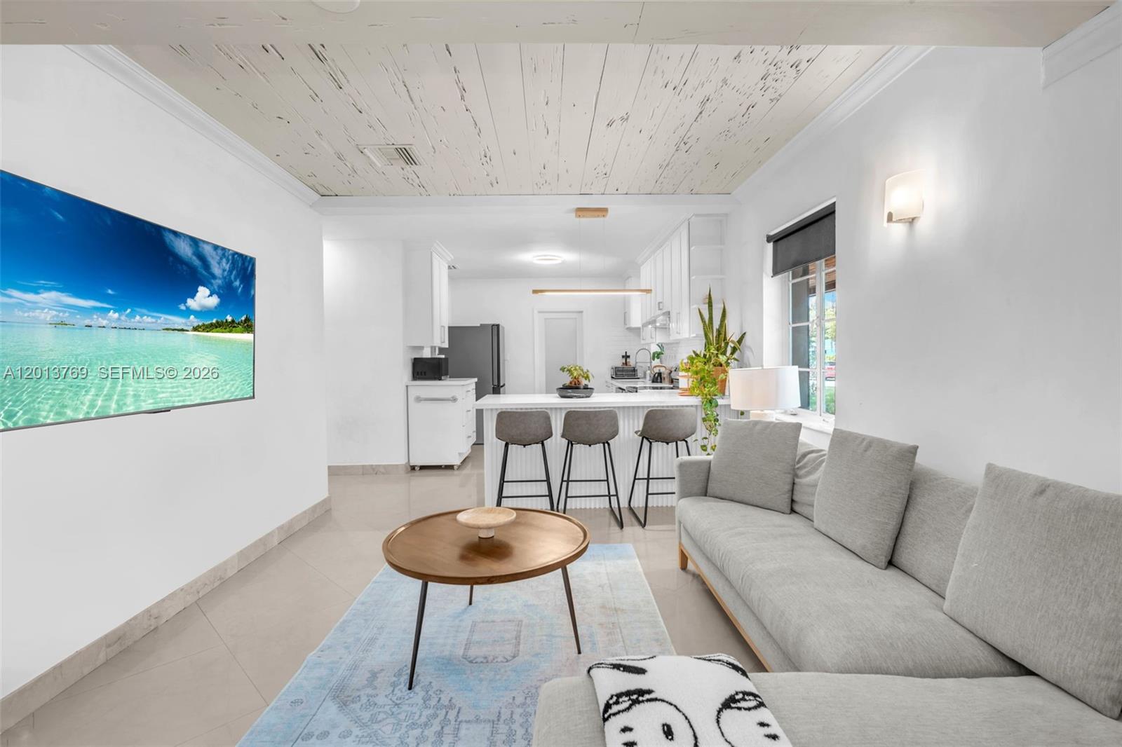 A living room with a white ceiling, gray sofa, and an open kitchen with bar seating — 470 NE 113th St # 1, Miami FL 33161, MIAMI, FL