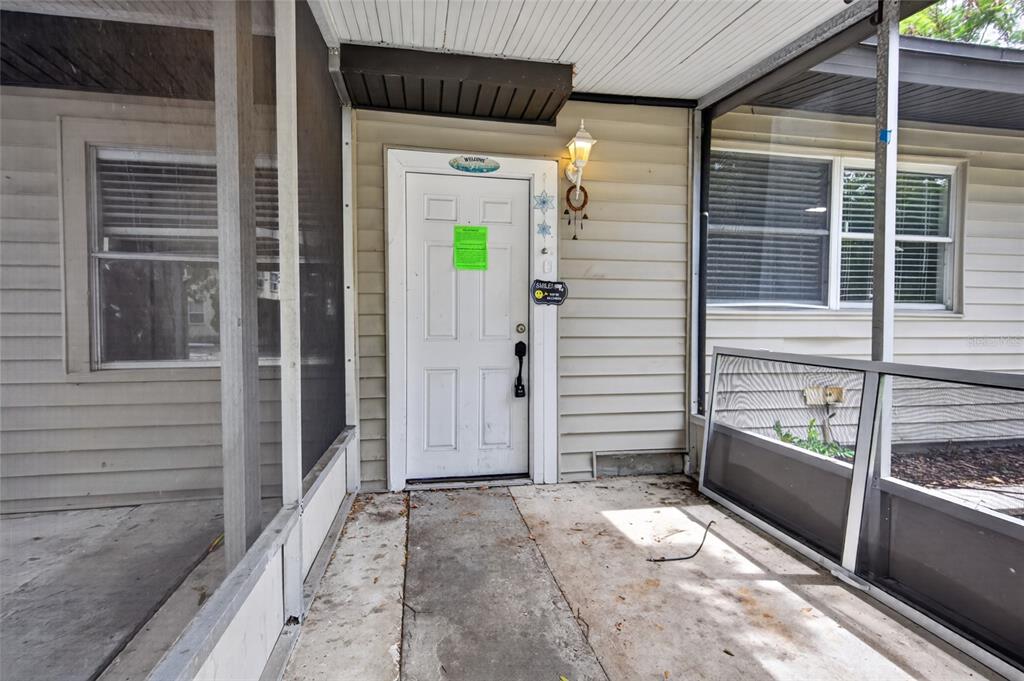 A white front door is centered on a screened-in porch with beige horizontal siding — 3615 W ROGERS AVENUE, TAMPA, FL