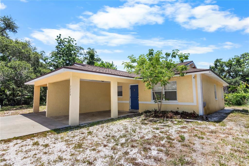 A yellow single-story house features a front carport, a blue door, and a gravel yard — 2228 25TH STREET UNIT 2228/2232, SARASOTA, FL