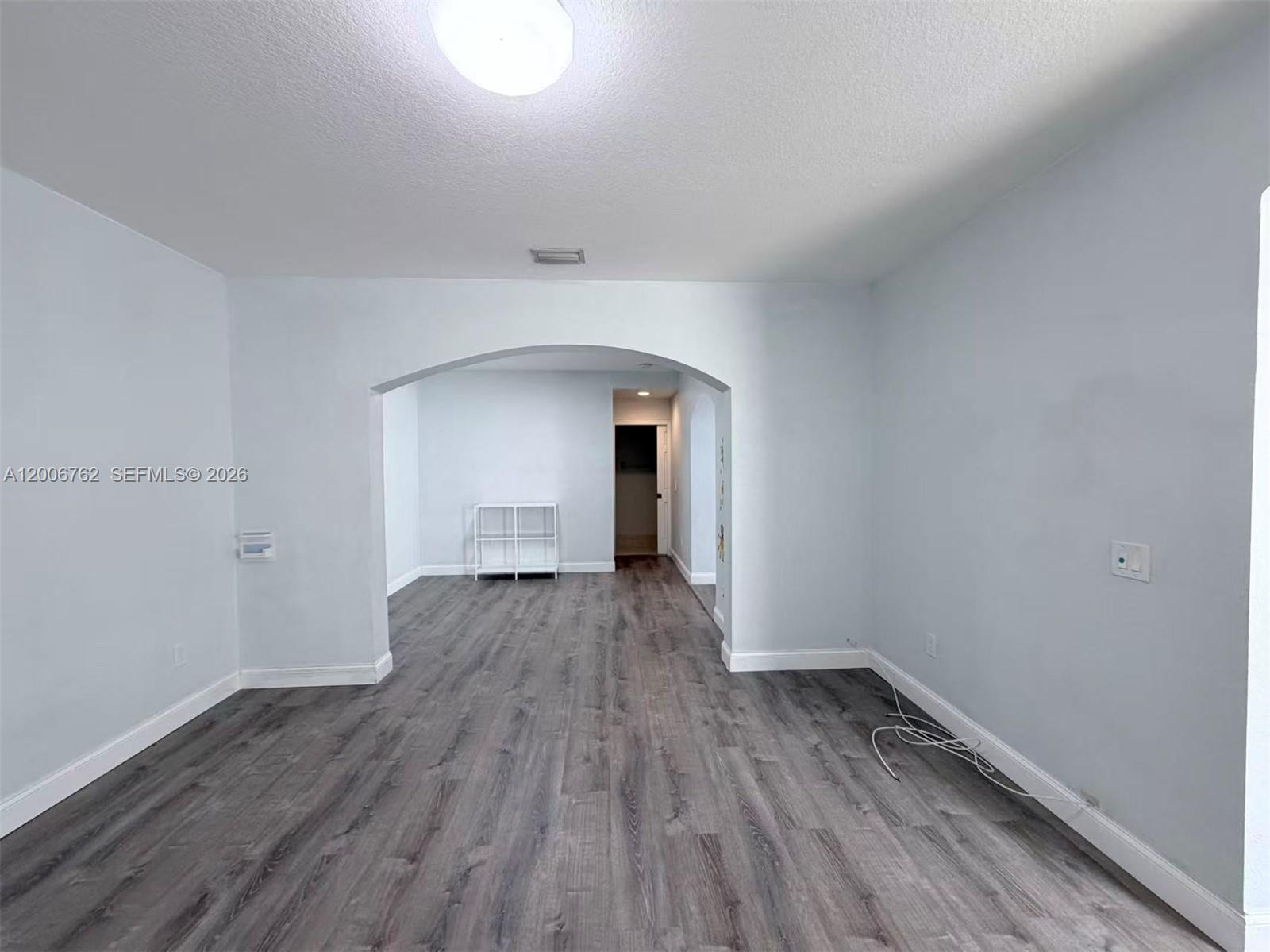 An empty room with gray wood-look flooring features an arched opening leading to another space — 15810 SW 40th St # 57, Miramar FL 33027, MIRAMAR, FL