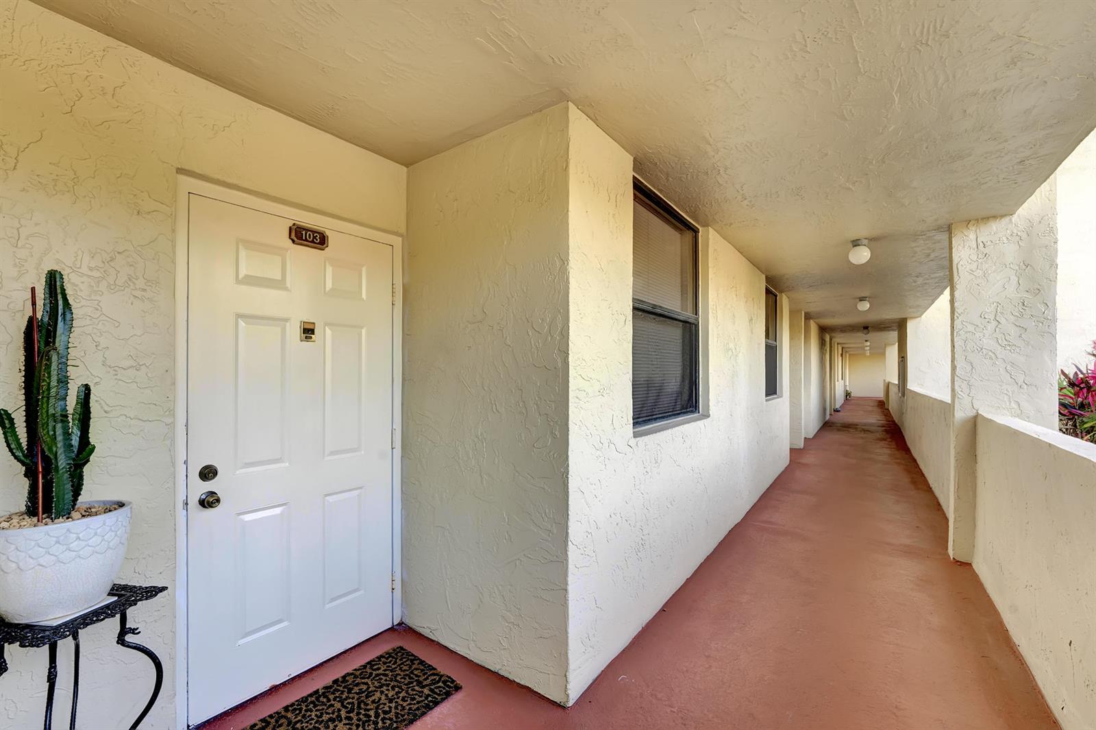 An exterior apartment hallway features a white door labeled 103, a potted cactus, and flooring — 1850 Homewood Boulevard # 1030, Delray Beach FL 33445, DELRAY BEACH, FL