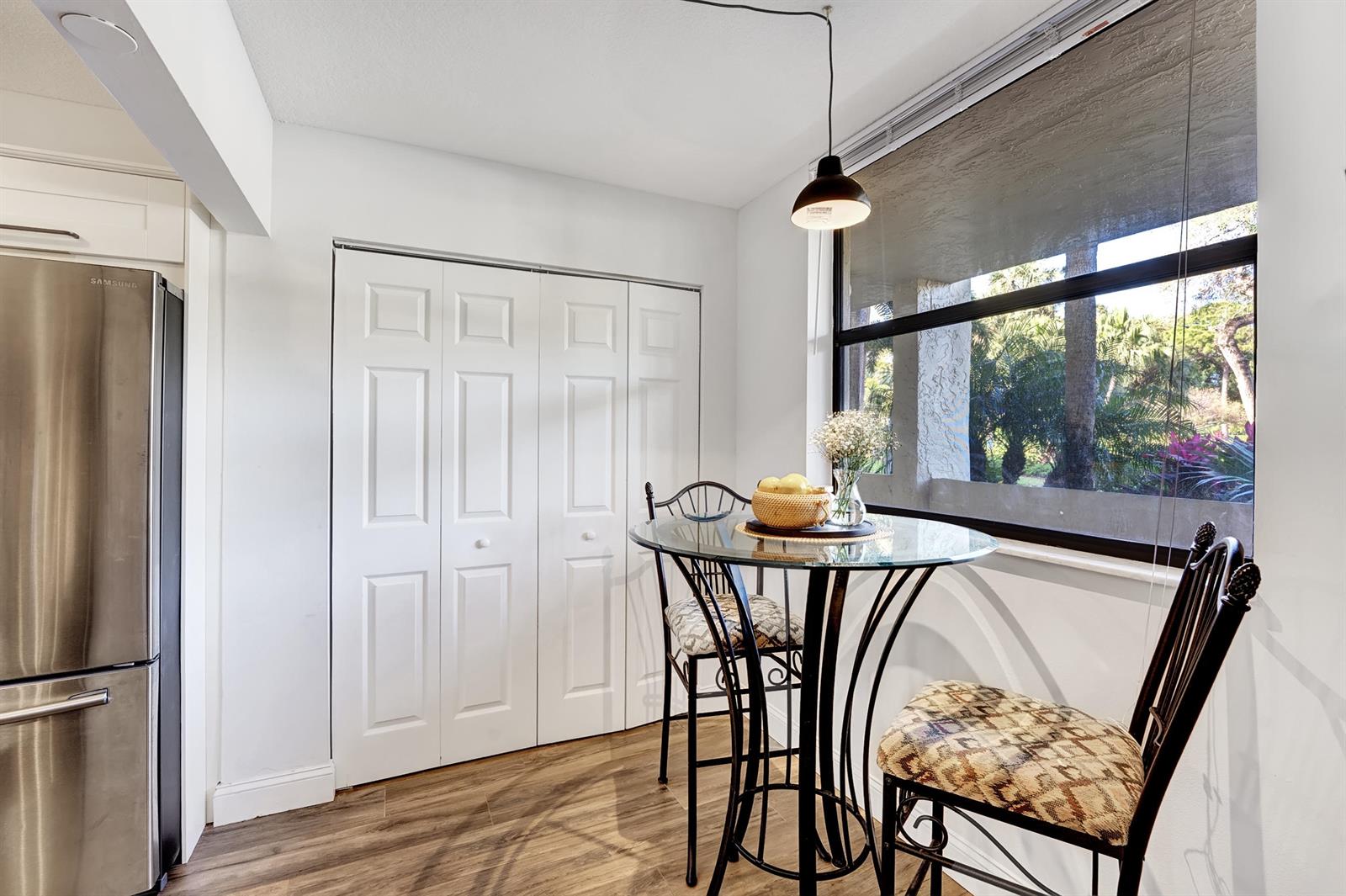 A dining nook features a glass-topped table, two chairs, a pendant light, and closet doors — 1850 Homewood Boulevard # 1030, Delray Beach FL 33445, DELRAY BEACH, FL