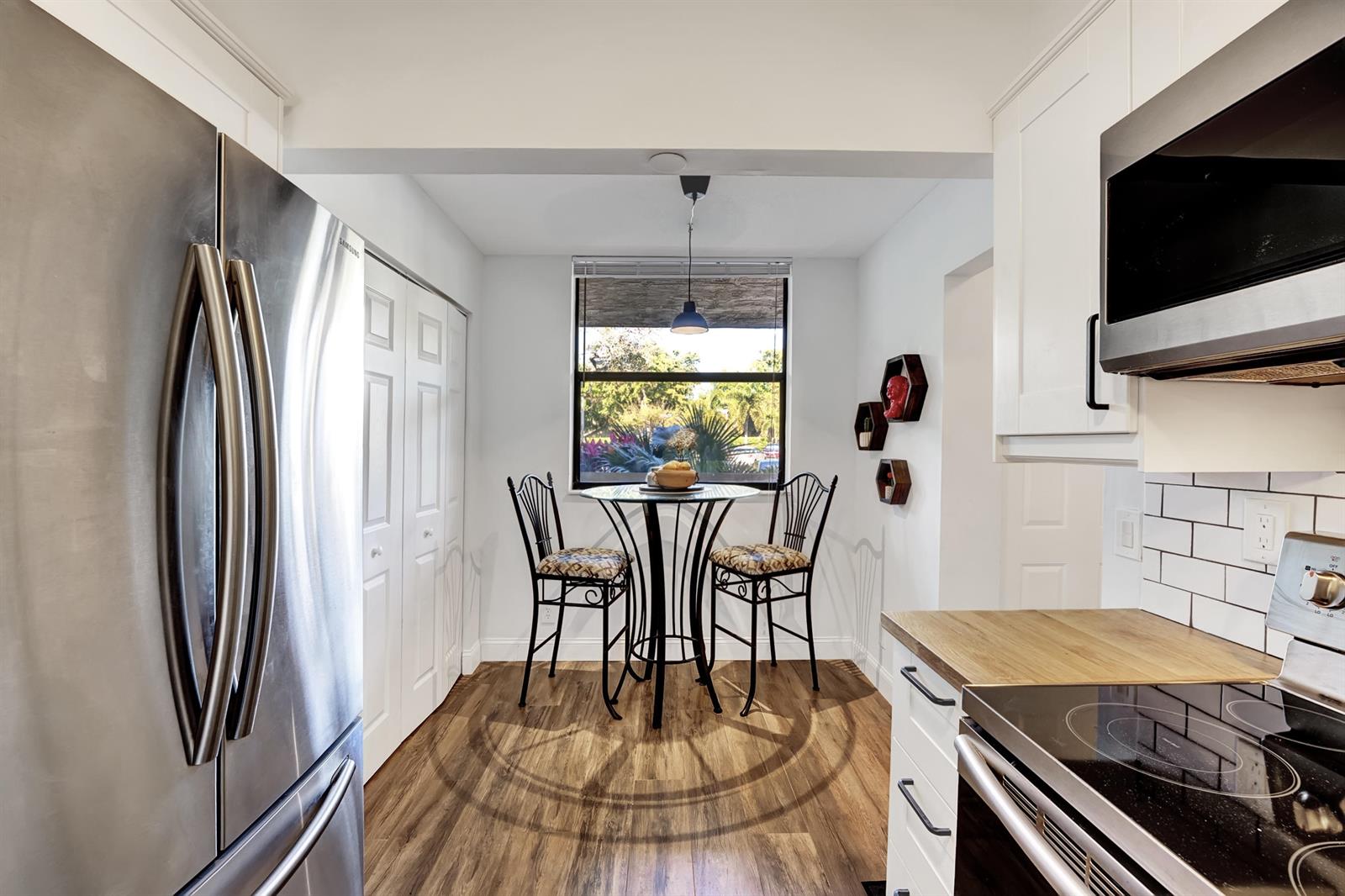 A kitchen with stainless steel appliances, white cabinets, wood-look flooring, and a small dining area — 1850 Homewood Boulevard # 1030, Delray Beach FL 33445, DELRAY BEACH, FL