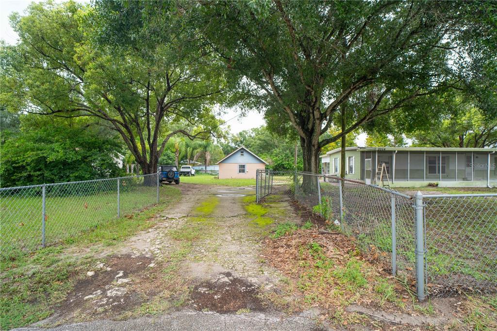 A gravel driveway leads between two large trees toward a small house behind a fence — 2014 GUNN HIGHWAY, ODESSA, FL