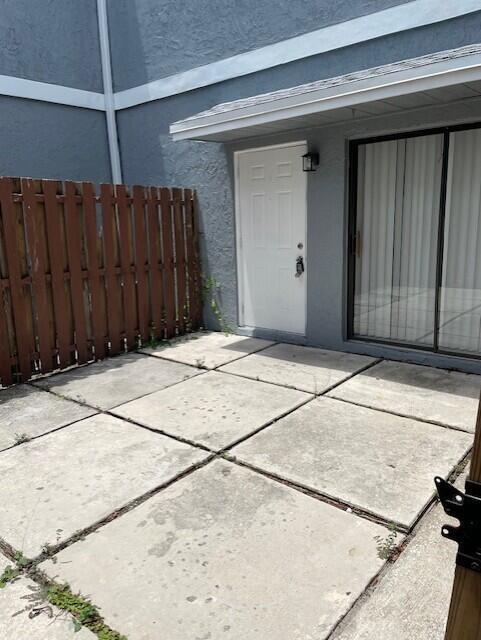 A concrete patio area features a white door and sliding glass doors against a building — 8 Crossings Circle # A, Boynton Beach FL 33435, BOYNTON BEACH, FL