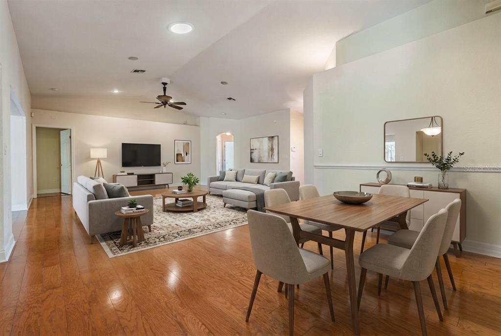 An open-concept living and dining area features hardwood floors, neutral furniture, and a vaulted ceiling — 10133 COLLAR DRIVE, SAN ANTONIO, FL