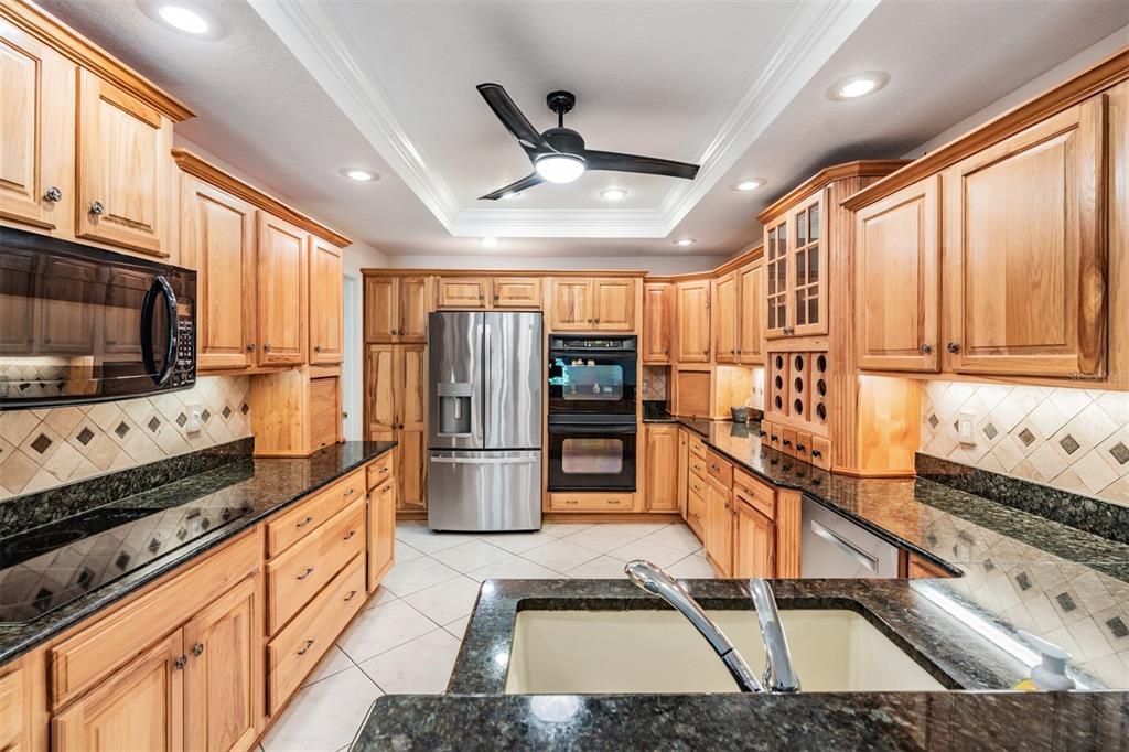 A kitchen with light wood cabinets, dark granite countertops, stainless steel appliances, and tile flooring — 10133 COLLAR DRIVE, SAN ANTONIO, FL