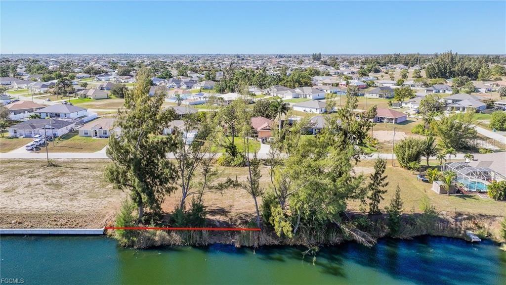 An aerial view shows a vacant waterfront lot with trees along a canal — 1235 NW 20TH PLACE, CAPE CORAL, FL