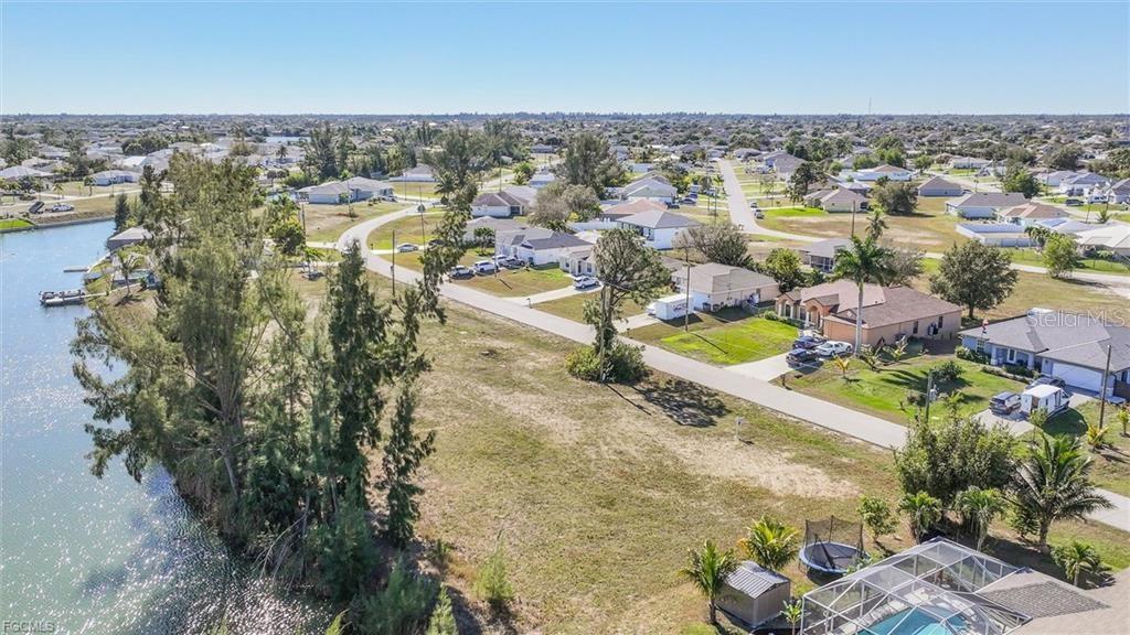 An aerial view shows a vacant grassy lot situated next to a canal and suburban houses — 1235 NW 20TH PLACE, CAPE CORAL, FL