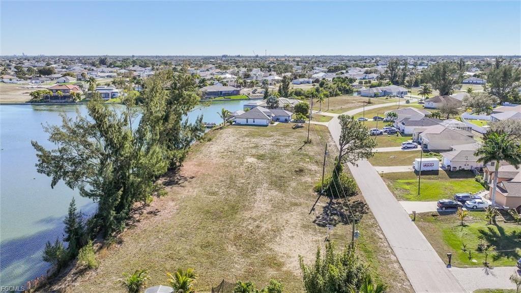 An aerial view shows a vacant waterfront lot situated next to a residential street — 1235 NW 20TH PLACE, CAPE CORAL, FL