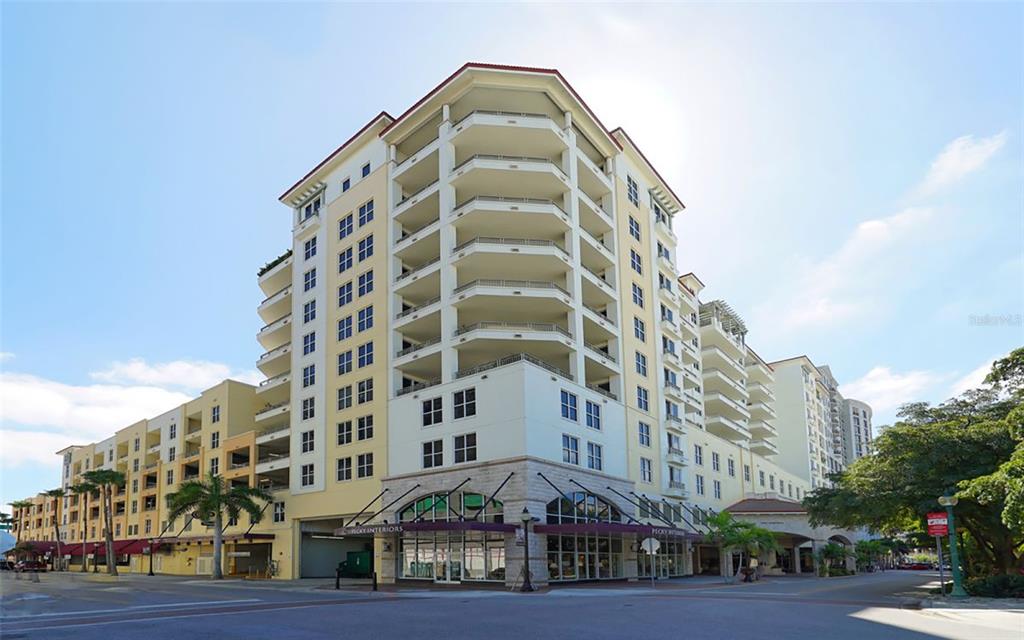 A multi-story apartment building with balconies and ground-level storefronts sits on a street corner — 100 CENTRAL AVENUE UNIT K817, SARASOTA, FL