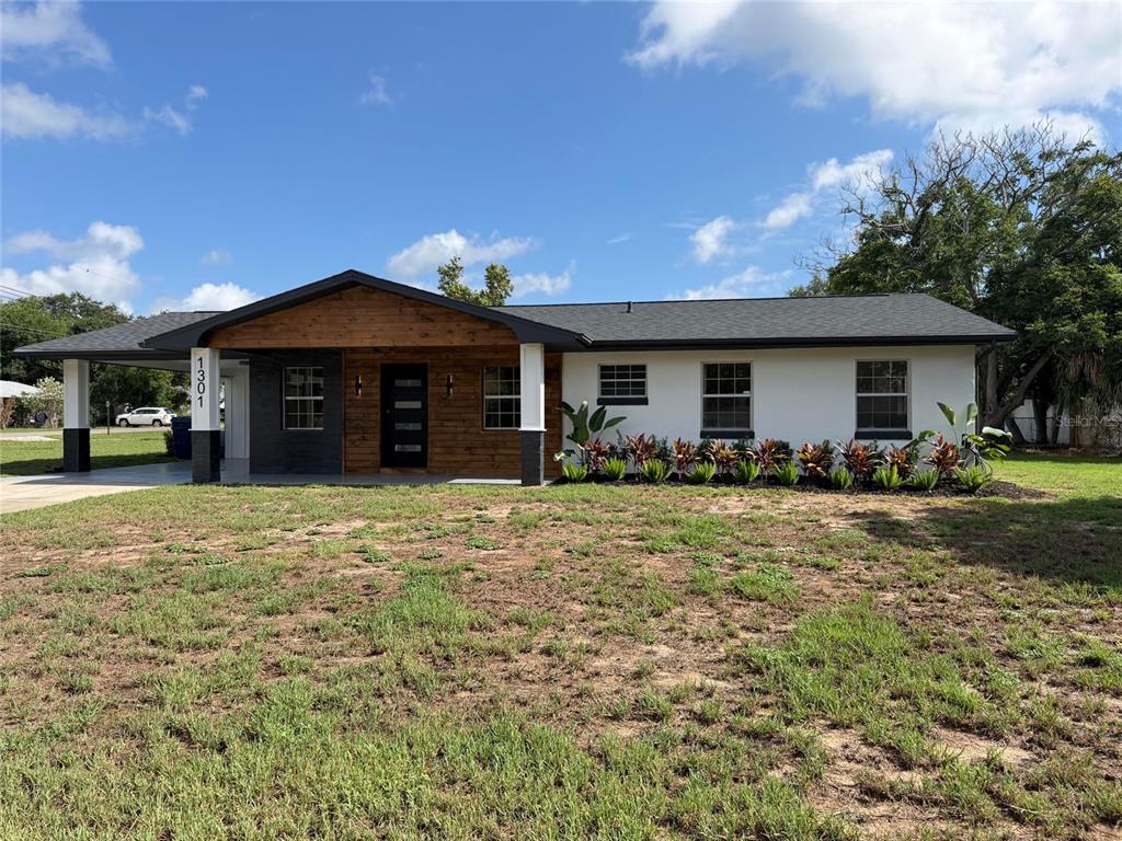 A single-story house with a wood-paneled entryway, white stucco walls, and a covered carport — 1301 NICHOLS DRIVE, TAVARES, FL