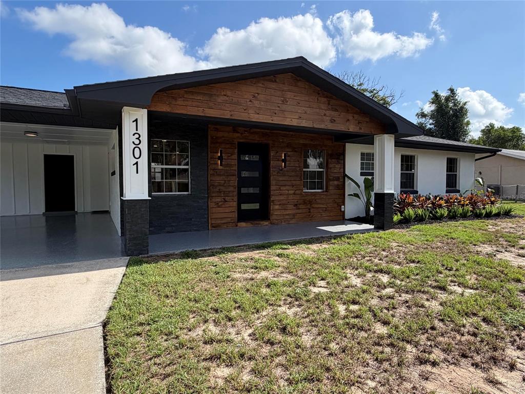 A modern ranch-style house exterior features wood siding, stone accents, and a covered front porch — 1301 NICHOLS DRIVE, TAVARES, FL