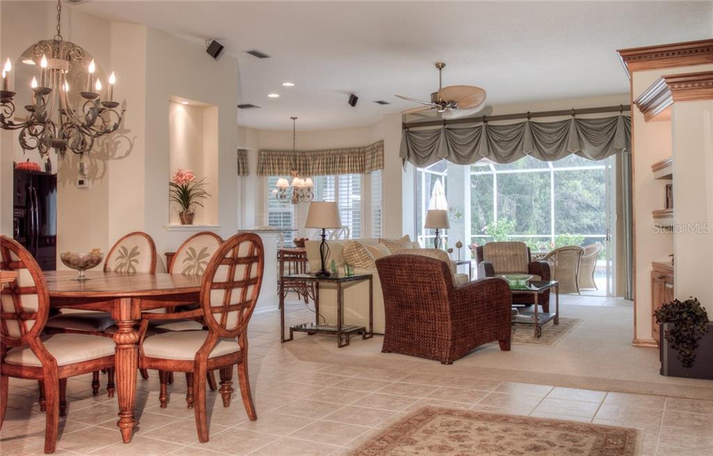 A dining area with a chandelier opens into a living room with a view of a pool — 6939 LENNOX PLACE, UNIVERSITY PARK, FL