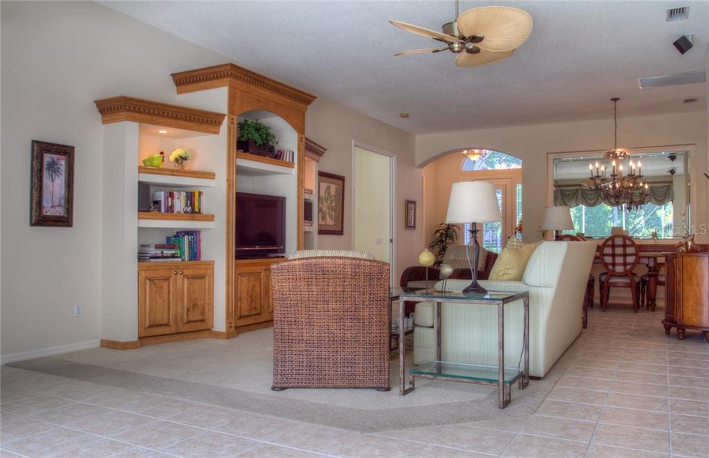 A living room with a built-in wooden entertainment center, wicker chair, and light-colored sofa — 6939 LENNOX PLACE, UNIVERSITY PARK, FL