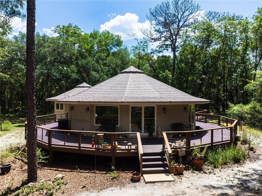 A round house with a wrap-around wooden deck sits in a wooded area — 13797 NE 199TH STREET, WALDO, FL