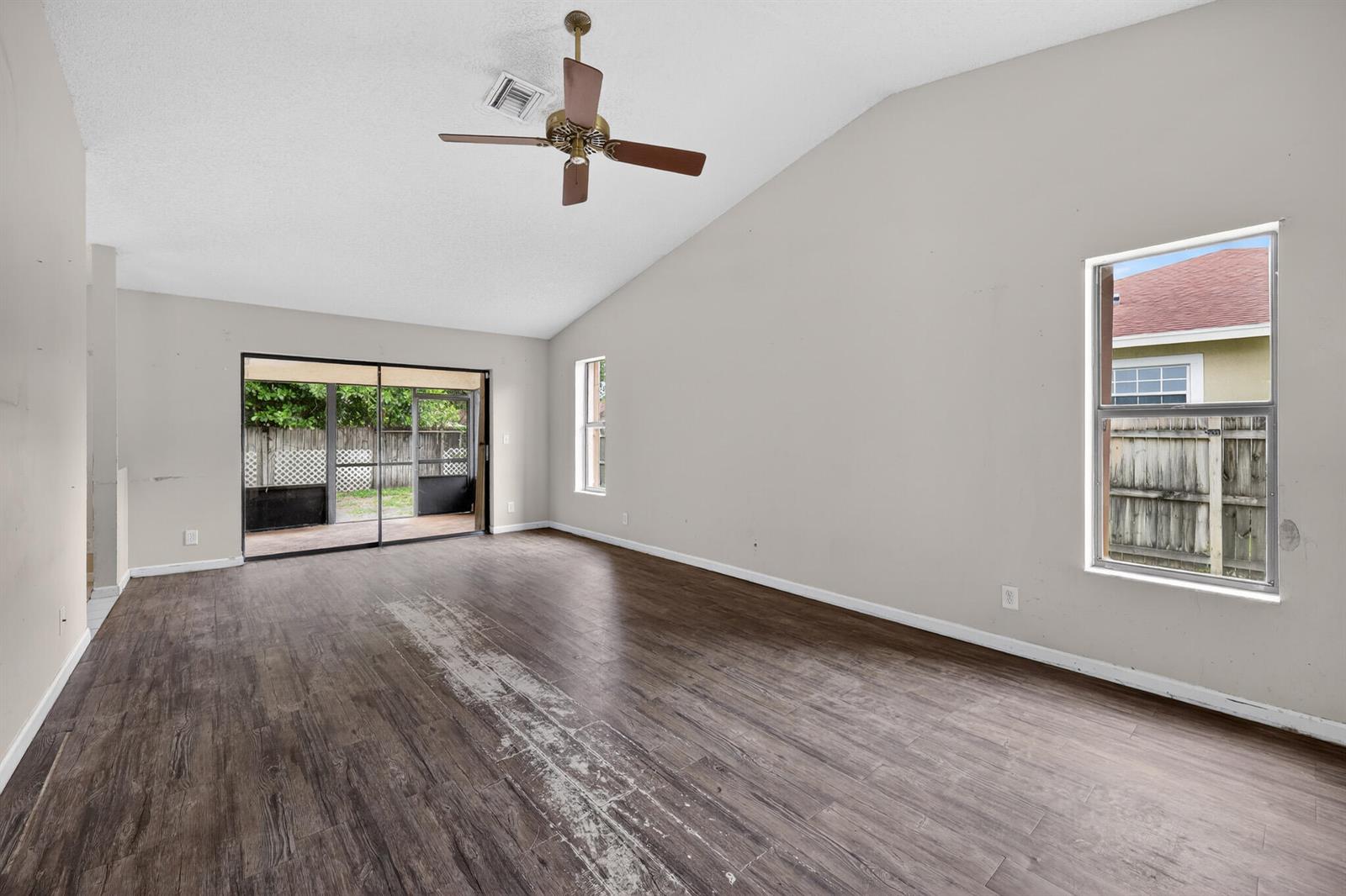 An empty living room features vaulted ceilings, a ceiling fan, sliding glass doors, and worn flooring — 14798 Paddock Drive, Wellington FL 33414, WELLINGTON, FL
