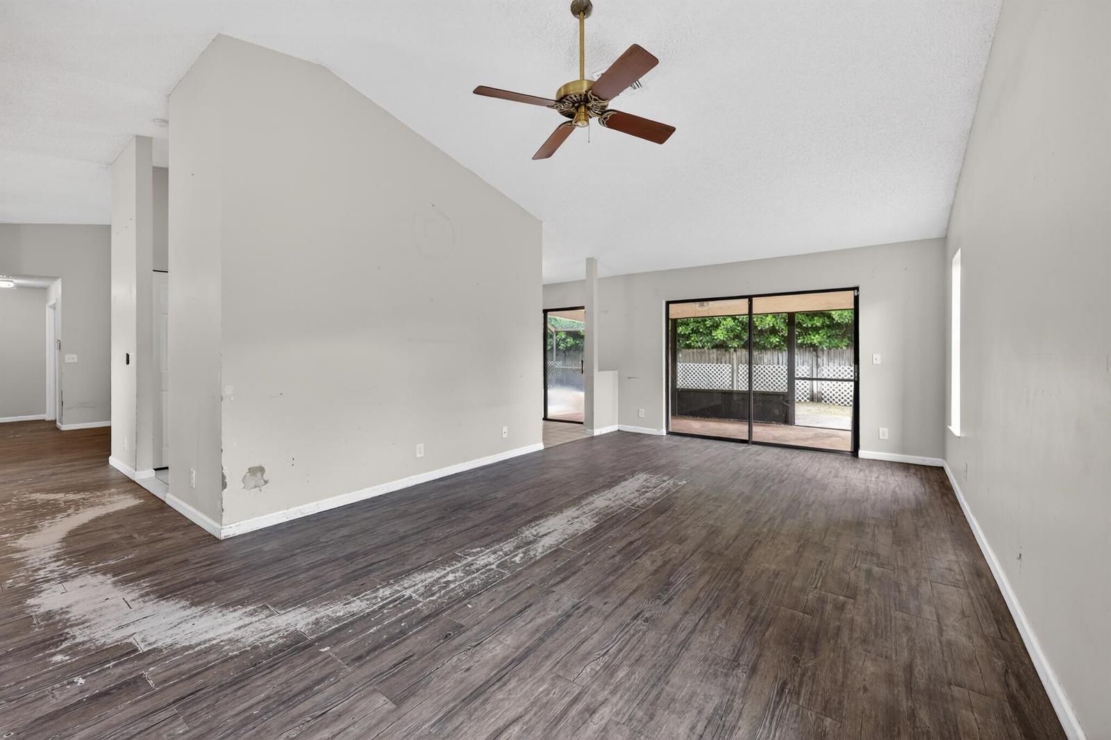An empty living room features dark wood-look flooring, a ceiling fan, and sliding glass doors — 14798 Paddock Drive, Wellington FL 33414, WELLINGTON, FL