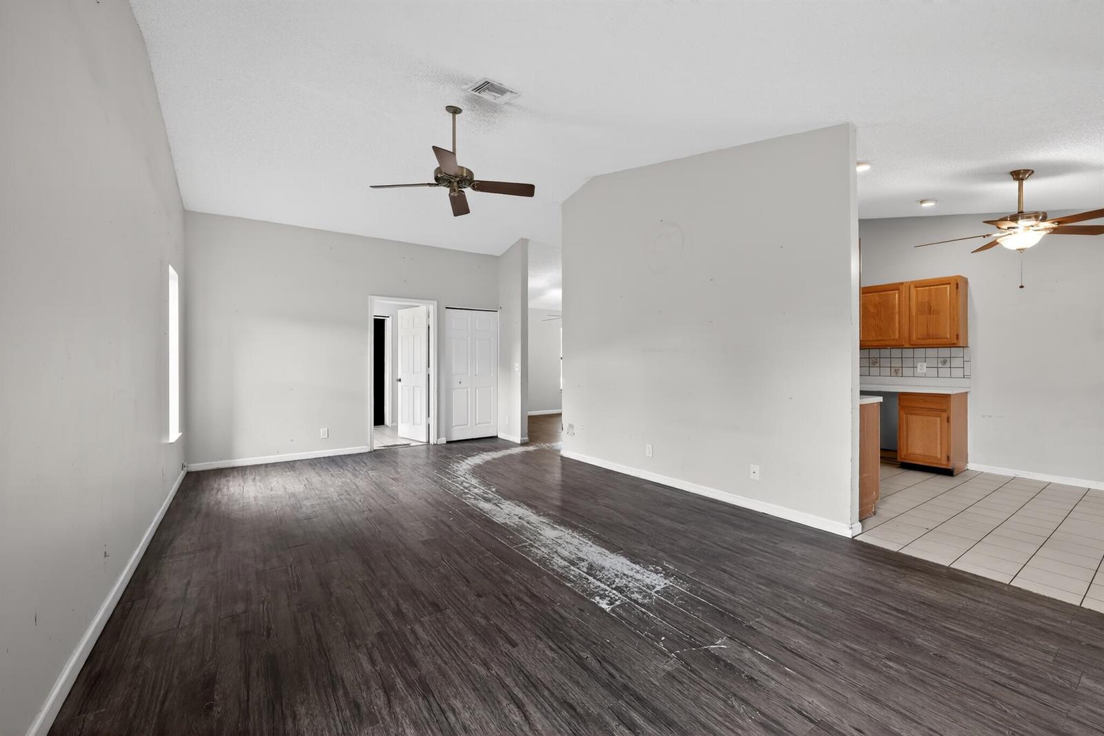 A living room with dark wood-look flooring, a ceiling fan, and an adjacent tiled kitchen — 14798 Paddock Drive, Wellington FL 33414, WELLINGTON, FL
