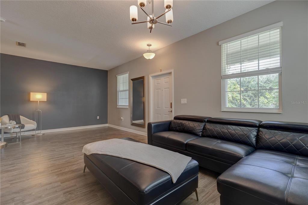 A living room features a black leather sectional, wood-look flooring, and a dark accent wall — 15066 BOOK CLUB ROAD, WINTER GARDEN, FL
