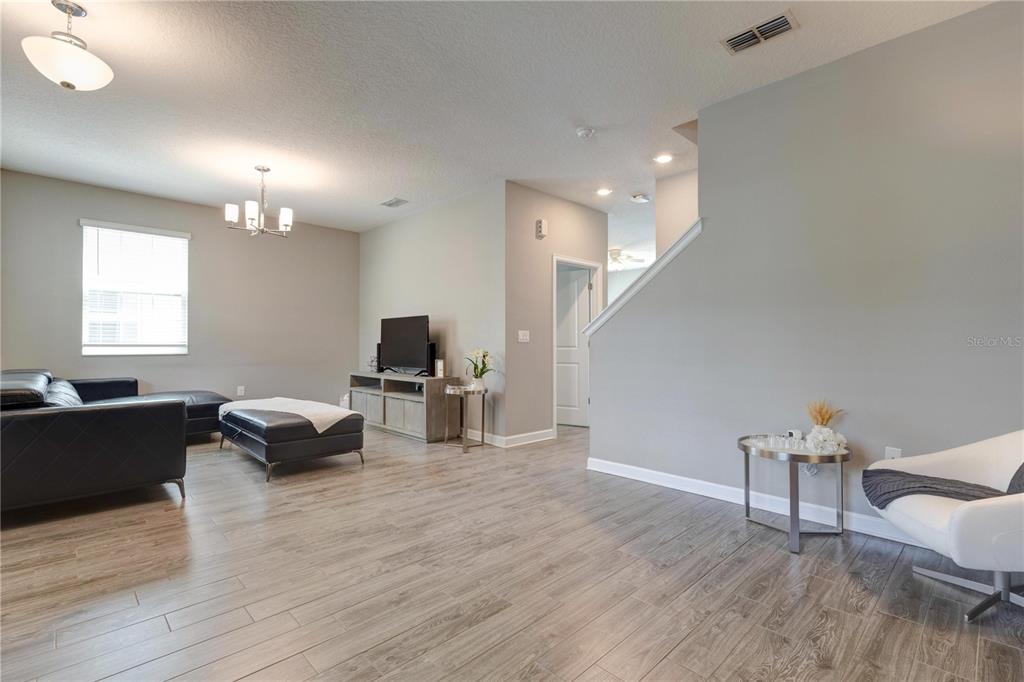 A living room features light wood-look flooring, gray walls, a black sectional, and a staircase — 15066 BOOK CLUB ROAD, WINTER GARDEN, FL