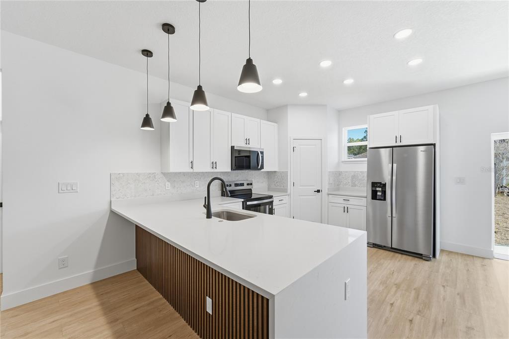 A modern kitchen features white cabinets, a quartz island with wood slats, and stainless appliances — 7109 N TAVOLI TERRACE, CITRUS SPRINGS, FL