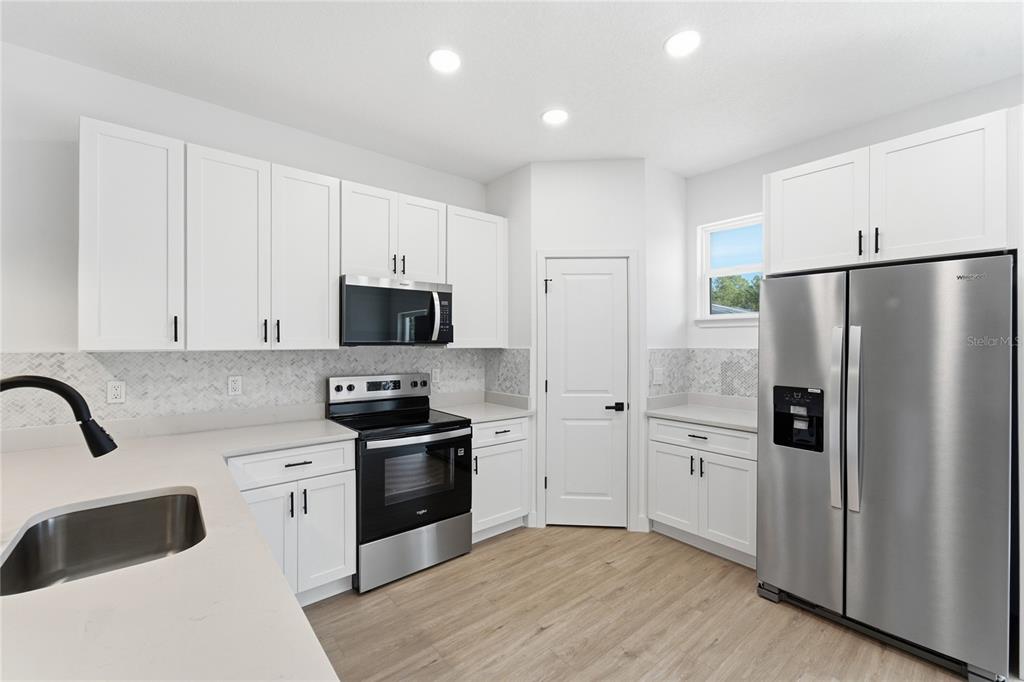 A modern kitchen features white cabinets, stainless steel appliances, light countertops, and wood-look flooring — 7109 N TAVOLI TERRACE, CITRUS SPRINGS, FL