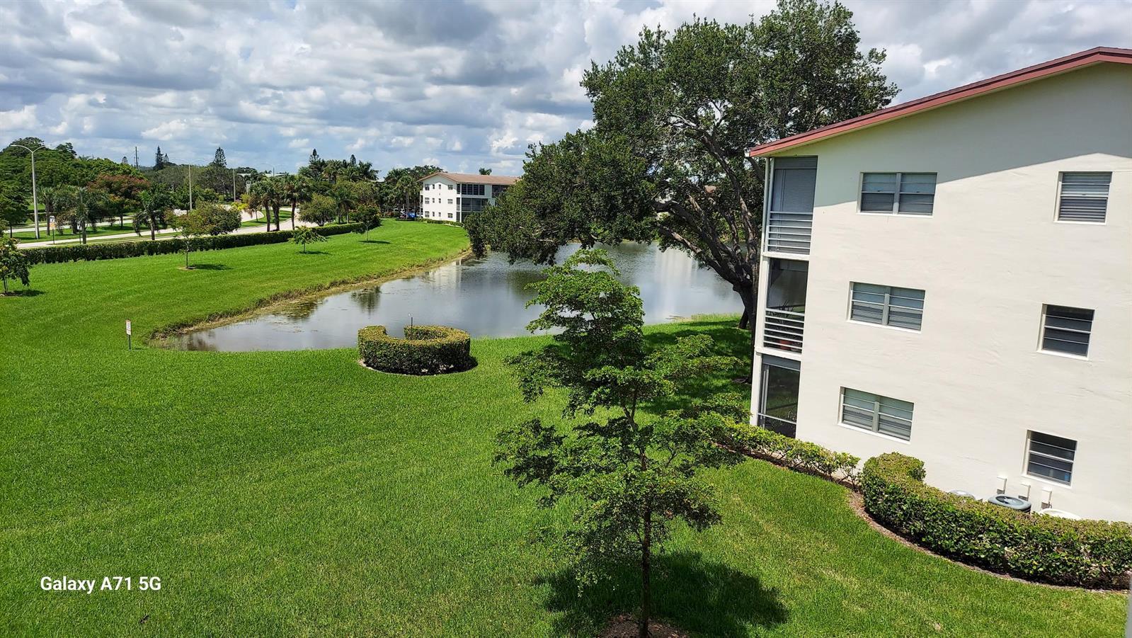 An exterior view of a multi-story apartment building overlooking a pond and grassy lawn — 160 Preston D # 160, Boca Raton FL 33434, BOCA RATON, FL