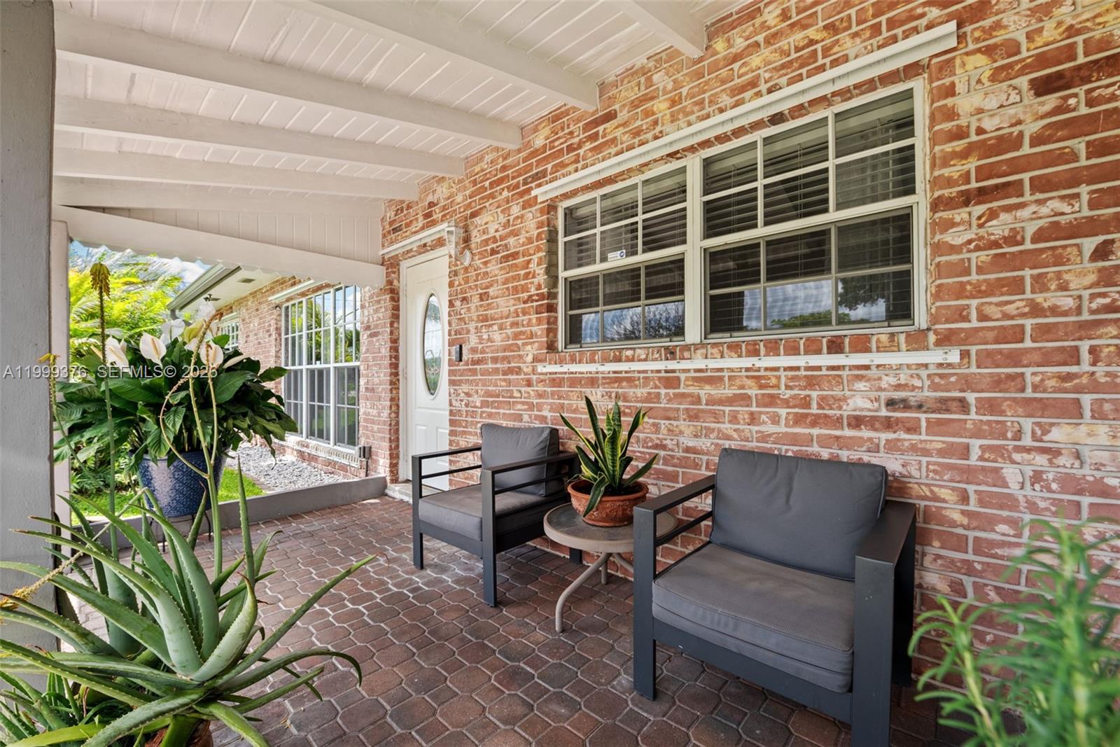 A covered brick patio features two gray chairs, a small table, and potted plants — 911 SW 51st Ave, Plantation FL 33317, PLANTATION, FL