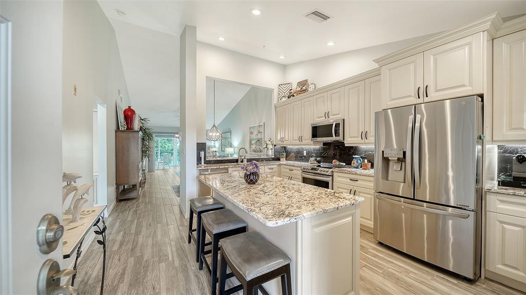 A kitchen with granite countertops, stainless steel appliances, and light cabinetry opens to a hallway — 8750 OLDE HICKORY AVENUE UNIT 9305, SARASOTA, FL