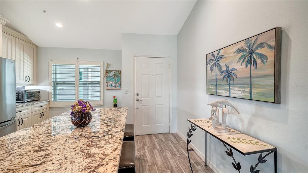 A kitchen with a granite island, white cabinets, and a console table with palm art — 8750 OLDE HICKORY AVENUE UNIT 9305, SARASOTA, FL