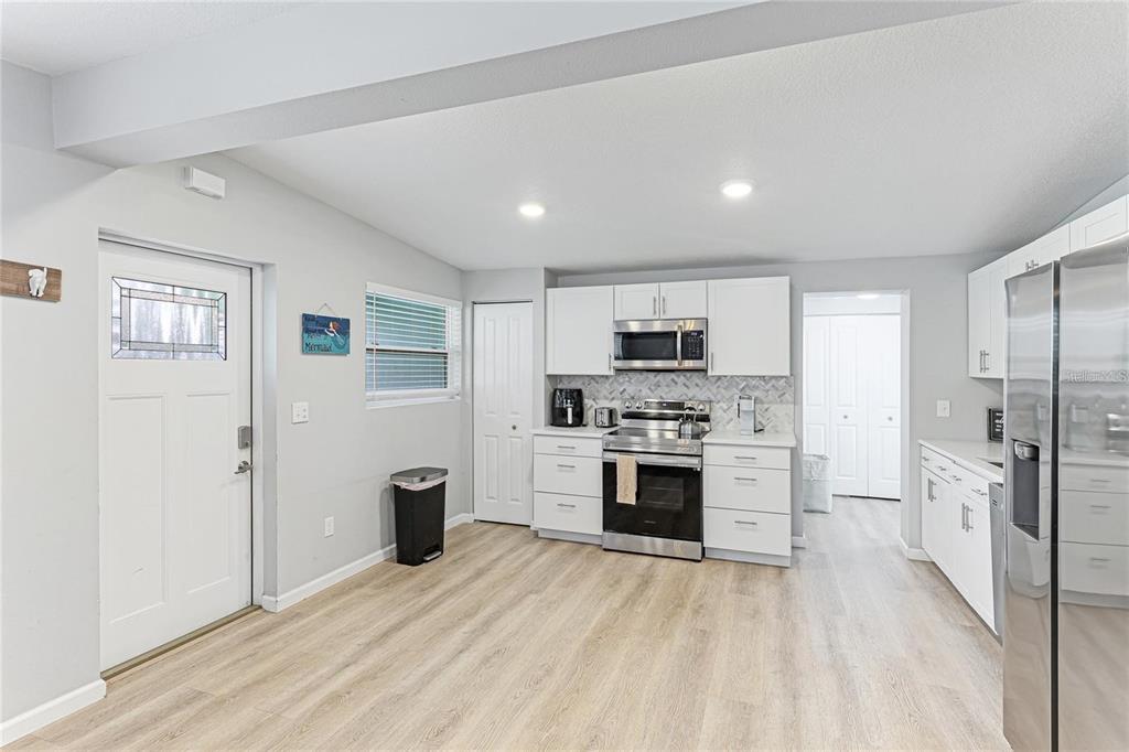 A kitchen features white cabinets, stainless steel appliances, light wood-look flooring, and a side door — 1023 ROBERTA STREET, VENICE, FL