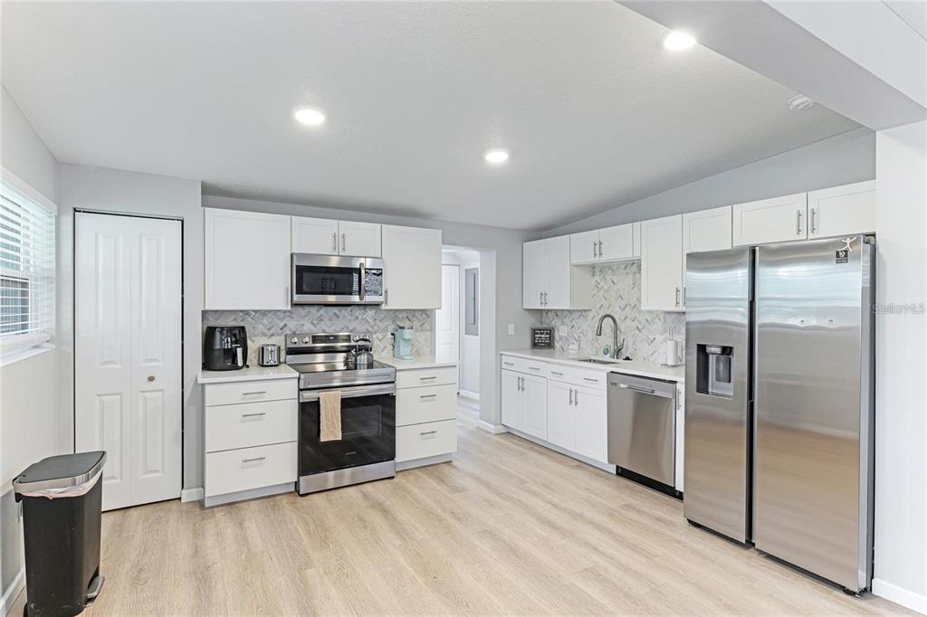 A kitchen features white cabinets, stainless steel appliances, a tiled backsplash, and light wood flooring — 1023 ROBERTA STREET, VENICE, FL