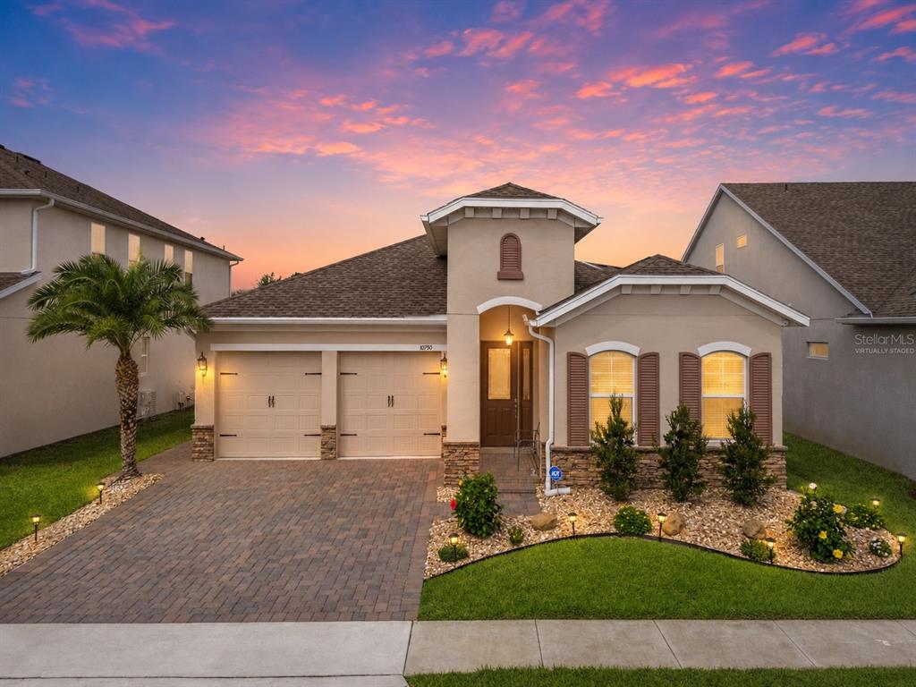 A single-story suburban house with a two-car garage, stone accents, and a paved driveway — 10750 PETRILLO WAY, WINTER GARDEN, FL