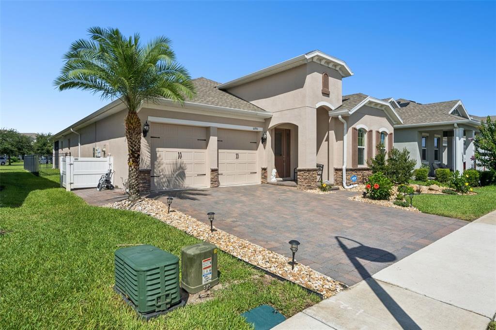 A single-story house with a two-car garage, stone accents, and a palm tree in front — 10750 PETRILLO WAY, WINTER GARDEN, FL