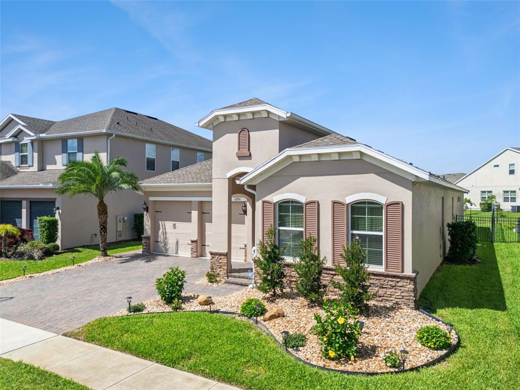 A single-story suburban house with a tan stucco exterior, stone accents, and a paved driveway — 10750 PETRILLO WAY, WINTER GARDEN, FL