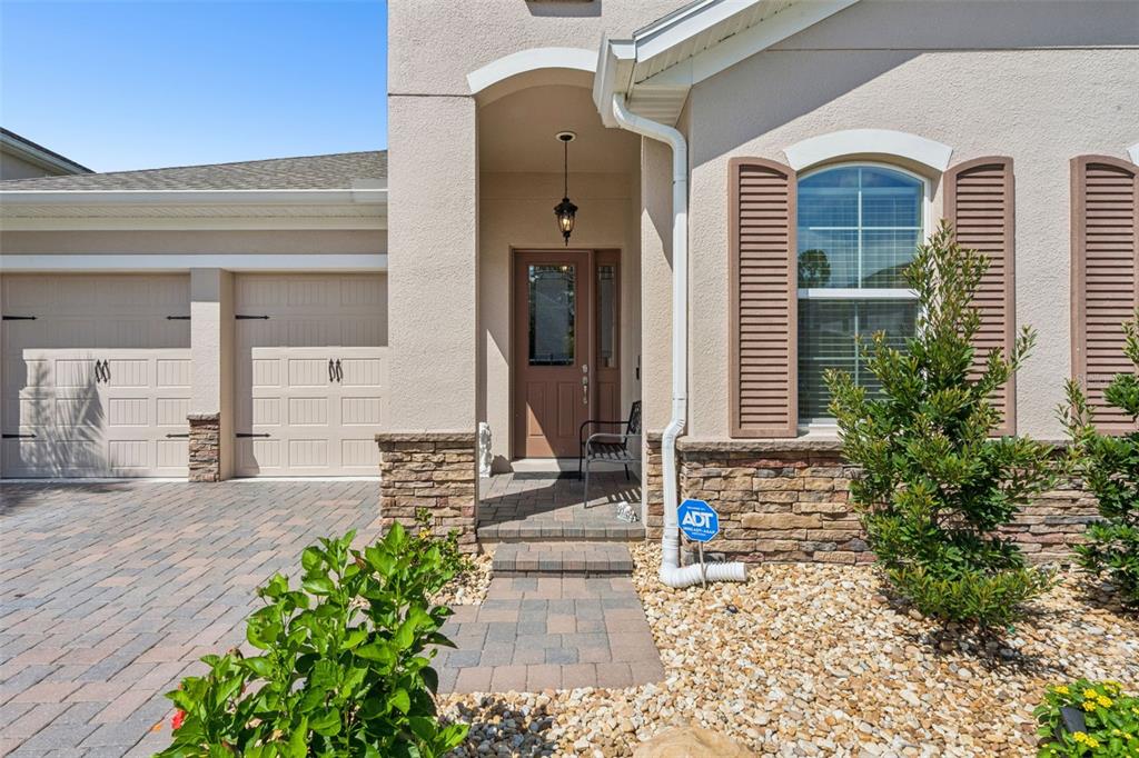 A beige house exterior features a stone-accented entryway, a paved driveway, and a garage — 10750 PETRILLO WAY, WINTER GARDEN, FL