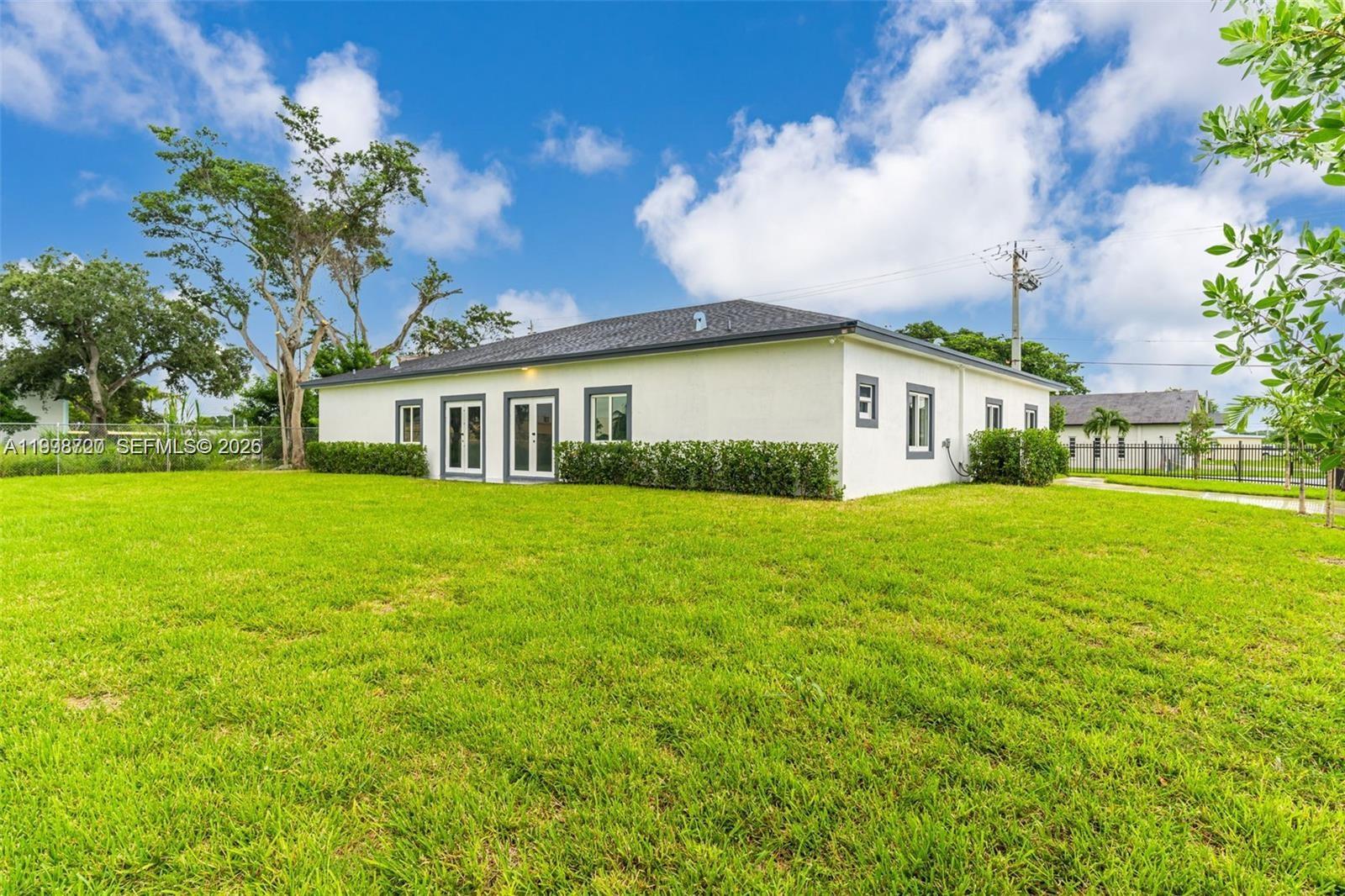 A white, single-story house with a dark roof sits on a large, grassy lawn — 11870 SW 220th St # A, Miami FL 33170, MIAMI, FL