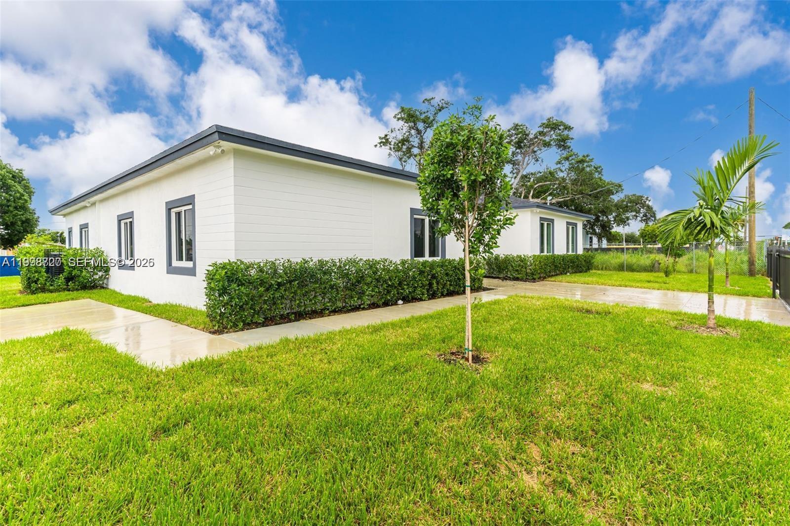 A white single-story house with dark trim sits on a grassy lot under a blue sky — 11870 SW 220th St # A, Miami FL 33170, MIAMI, FL