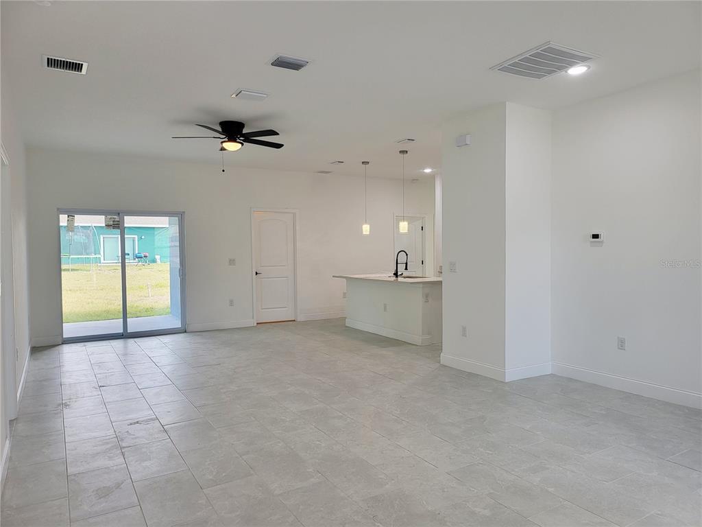 An open-concept living area features light-colored tile flooring, a kitchen island, and sliding glass doors — 415 TONKLIN ROAD SW, PALM BAY, FL