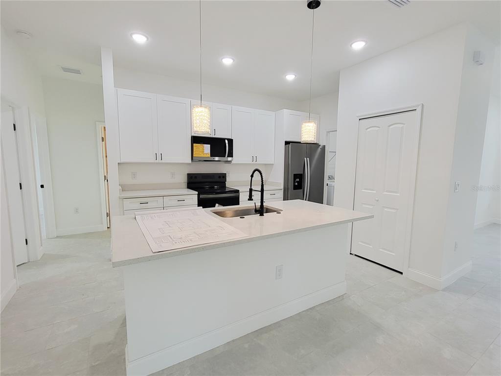 A modern kitchen features white cabinetry, a central island with a sink, and stainless appliances — 415 TONKLIN ROAD SW, PALM BAY, FL