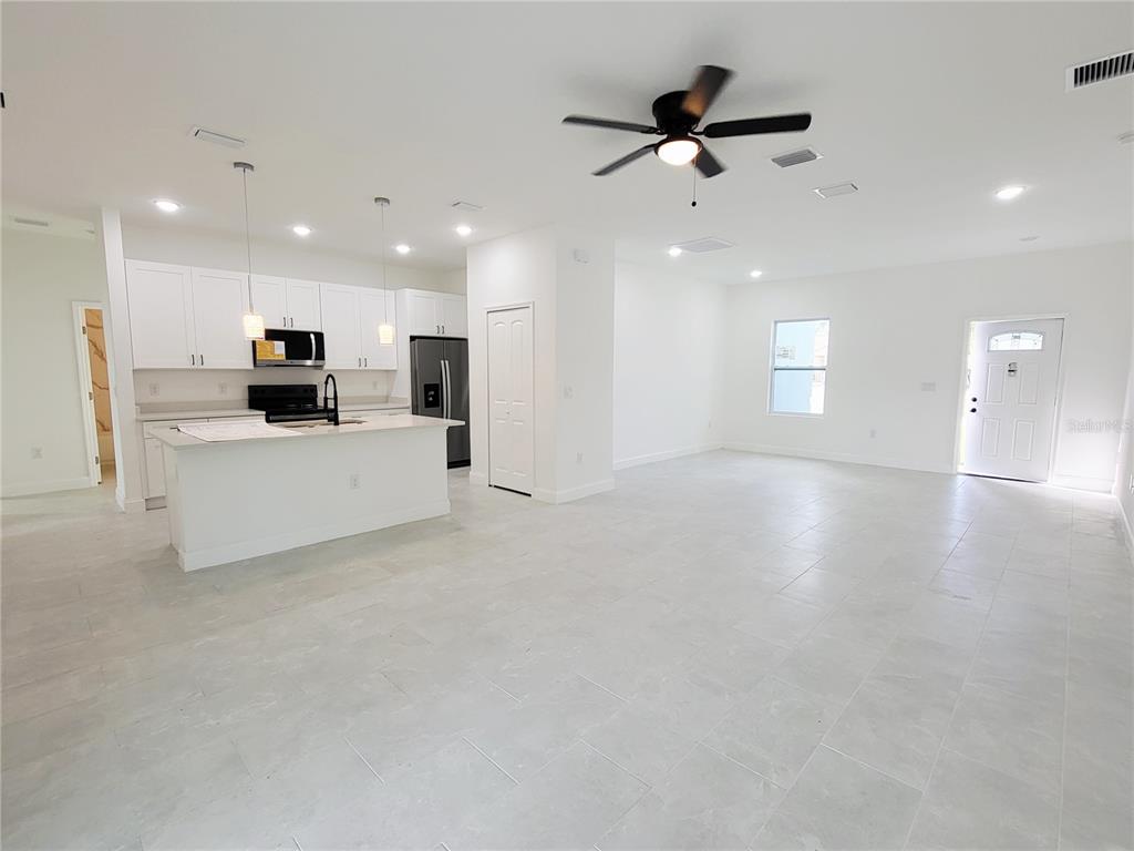 An open-concept kitchen and living area featuring white cabinets, stainless appliances, and tile flooring — 415 TONKLIN ROAD SW, PALM BAY, FL