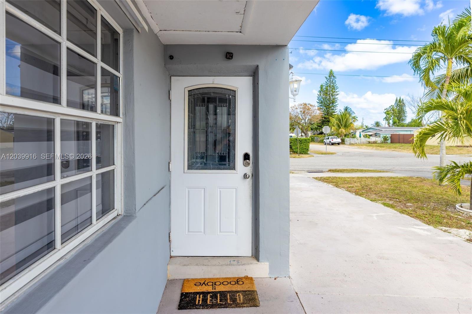 A white front door with a glass insert sits beside a window on a concrete porch — 6801 Park St # 6801, Hollywood FL 33024, HOLLYWOOD, FL
